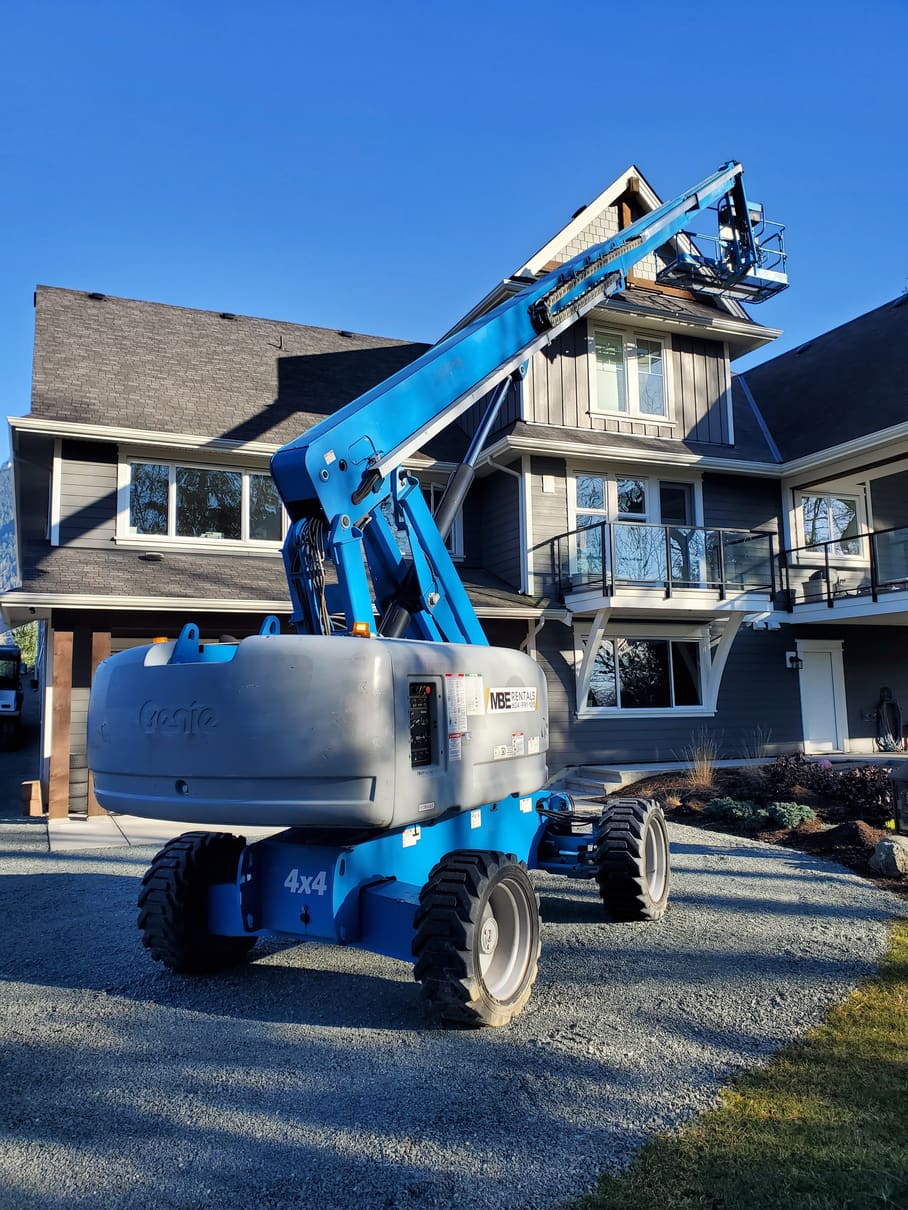 MBE Rentals Genie S-65 boom lift extended beside a two-storey house in Rosedale, BC